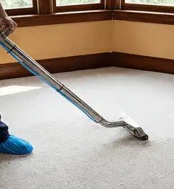 Steam carpet cleaning technician using a hot-water extraction wand on a residential carpet, wearing blue protective shoe covers Ann Arbor, MI.