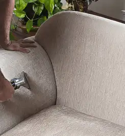Professional upholstery cleaner deep-cleaning a fabric sofa with a handheld extraction tool and hose Ann Arbor, MI.
