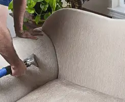 Professional upholstery cleaner deep-cleaning a fabric sofa with a handheld extraction tool and hose in Ann Arbor, MI.